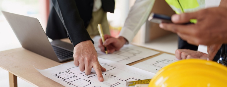 People working on paper architectural plans with computer, calculator and hardhat