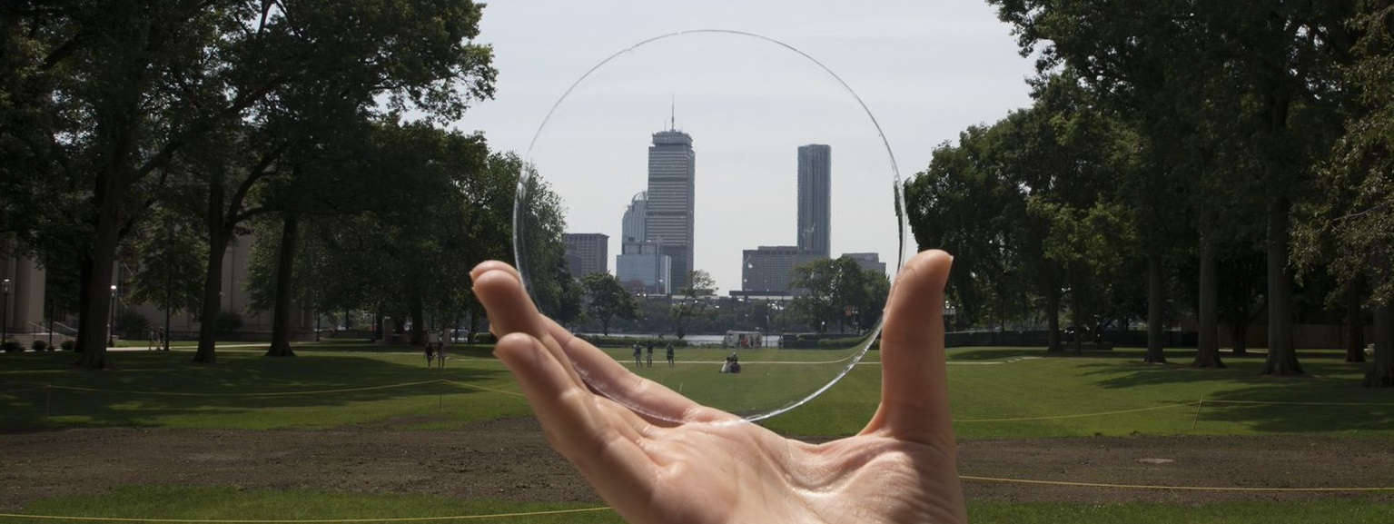 Hand holding clear disk with Boston skyline seen through it