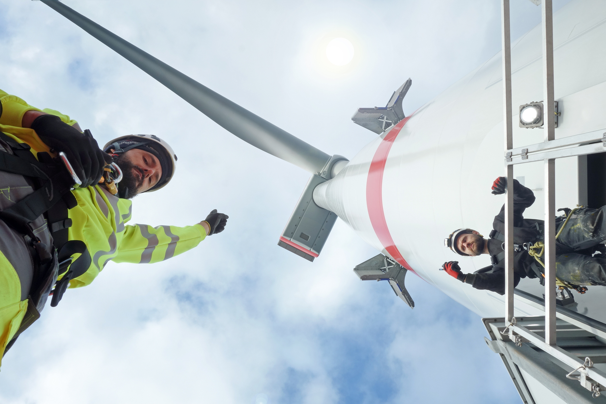 Upward view of workers in protective gear and wind turbine