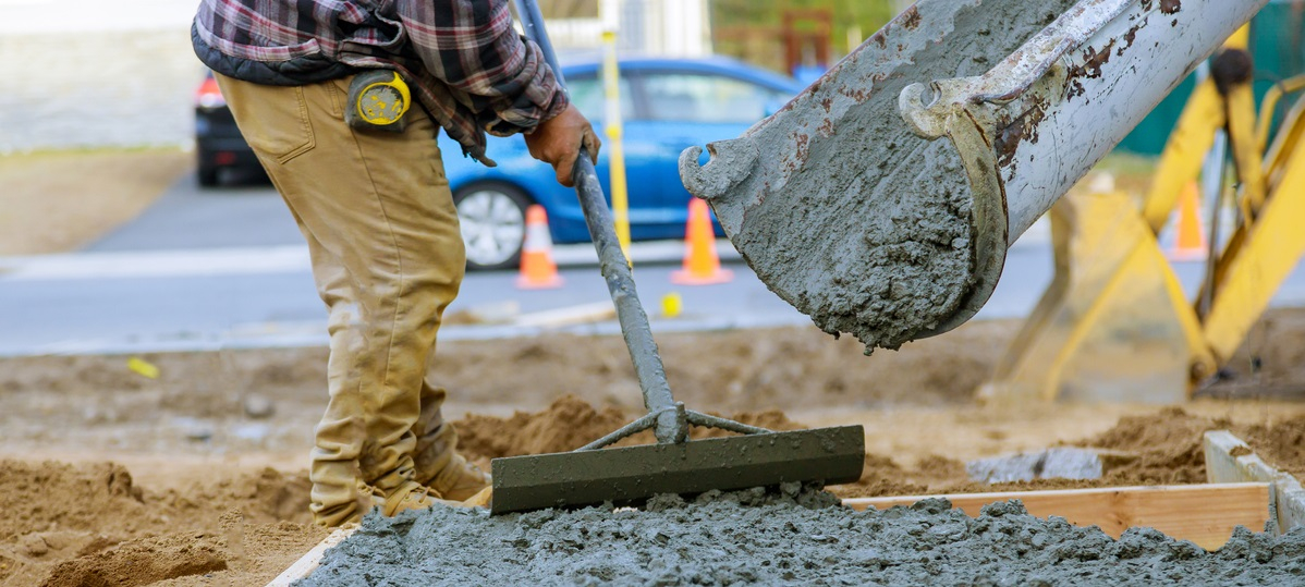 Concrete pouring onto construction site and being spread by worker