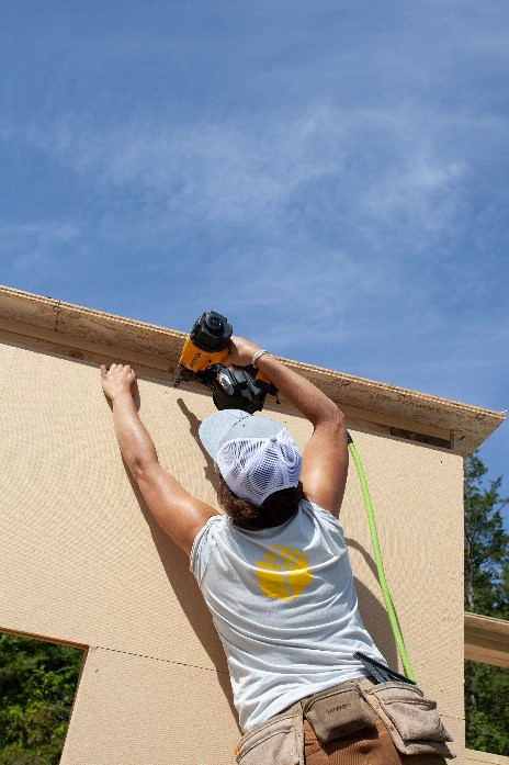 Person with nail gun working on residential roof.